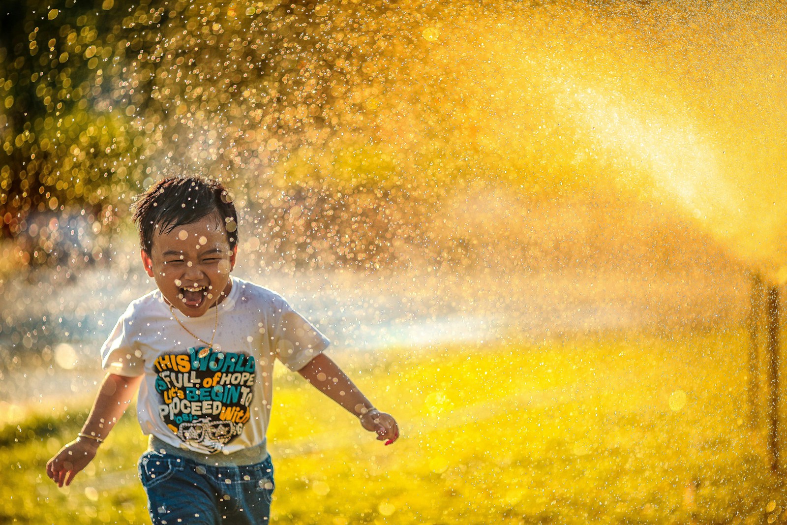 Photo by MI PHAM a young boy running through a sprinkle of water.