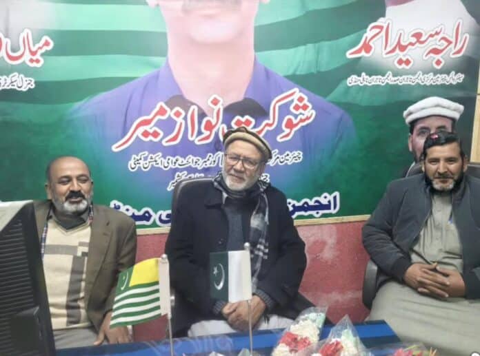 Two flags placed on a table during the inauguration of the Jammu Kashmir Joint Awami Action Committee office in Muzaffarabad, with committee members seated.