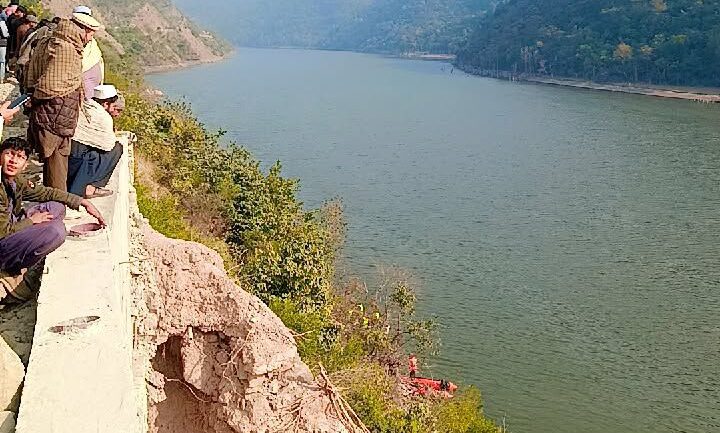 The spot where the van plunged into the dam, with stranded passengers sitting helplessly nearby watching the rescue efforts.